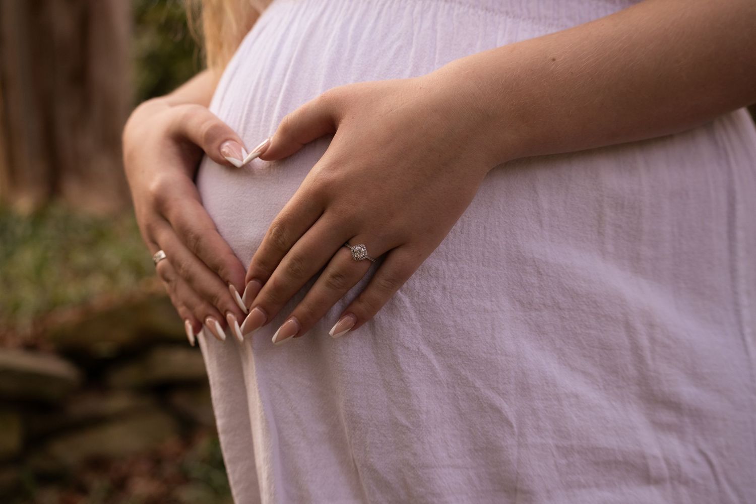 Close up of hands forming heart shape over pregnant belly.
