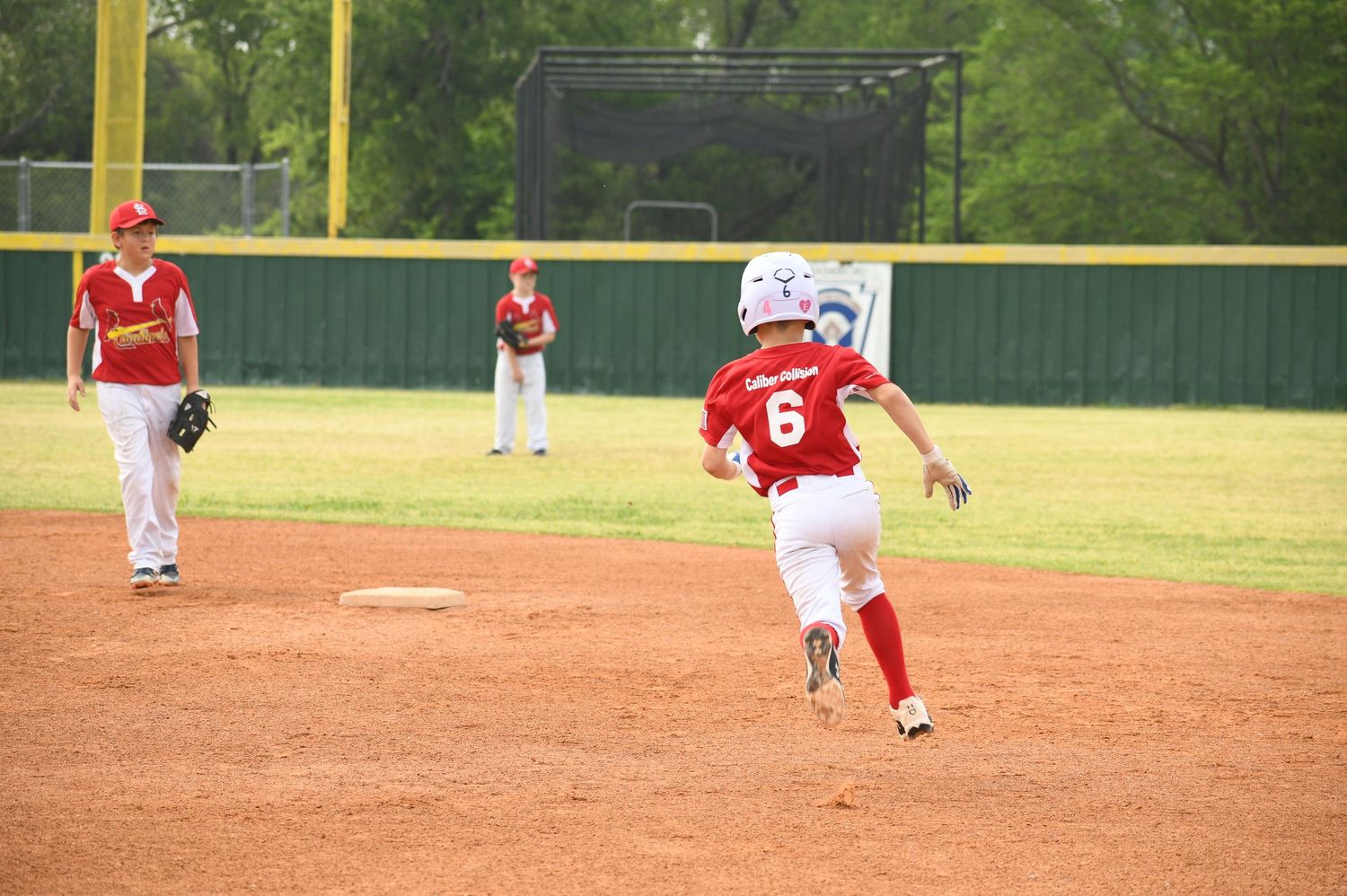 A baseball player in red uniform throws a pitch during a game on a sunny day at an outdoor diamond.