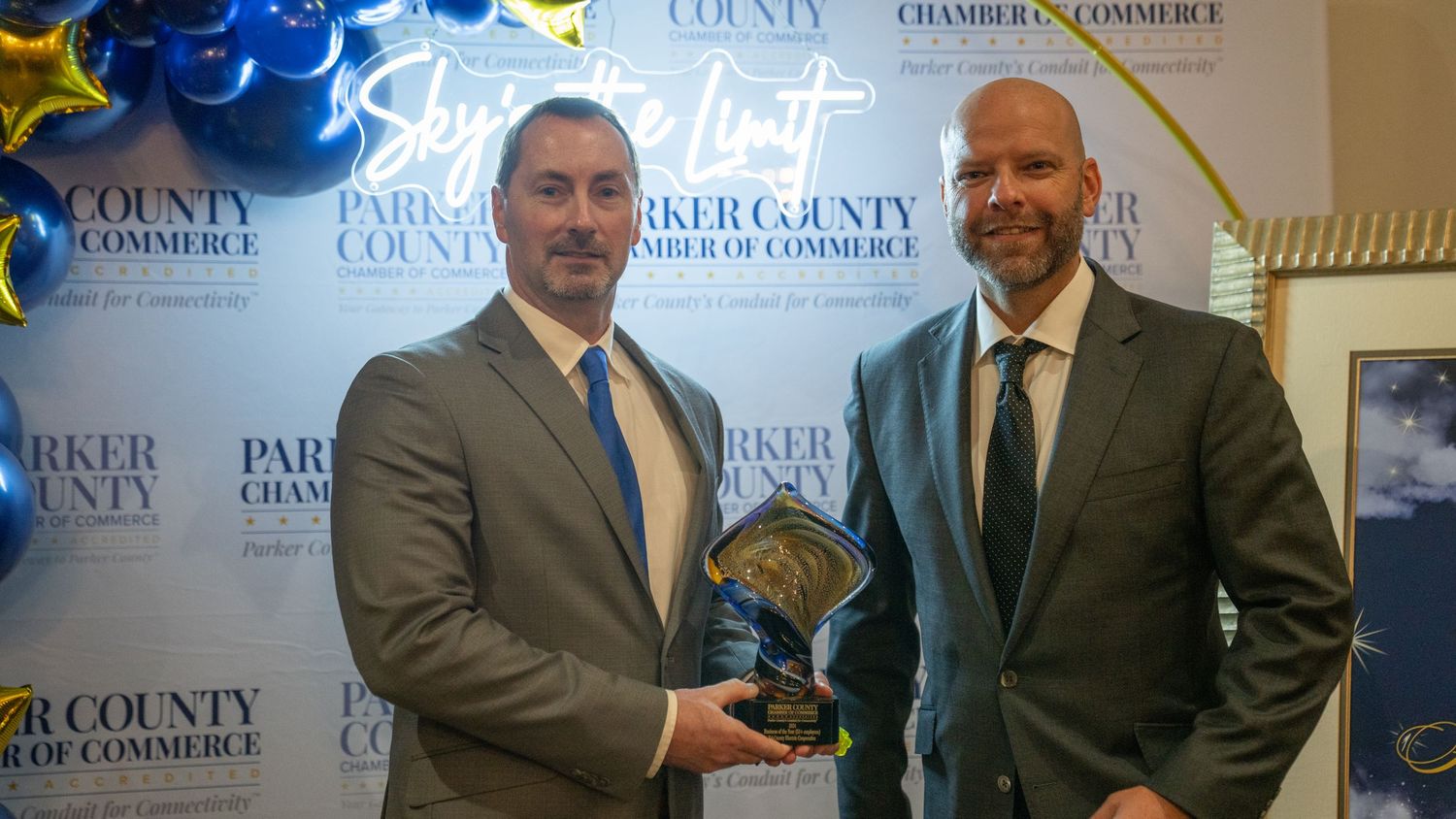 Two award recipients in suits hold trophy at Parker County Chamber celebration.