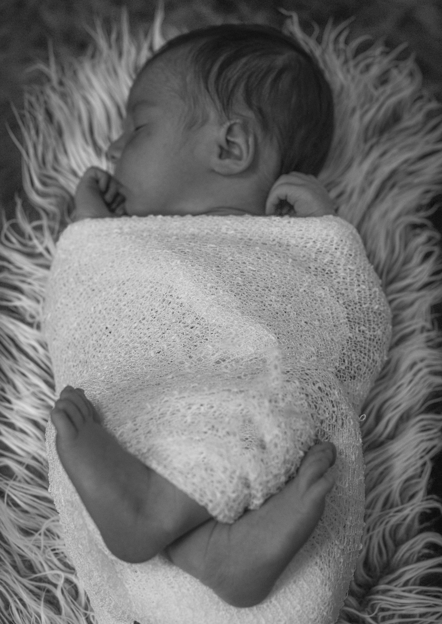 Newborn baby wrapped in white lace blanket sleeping on fluffy white fur.