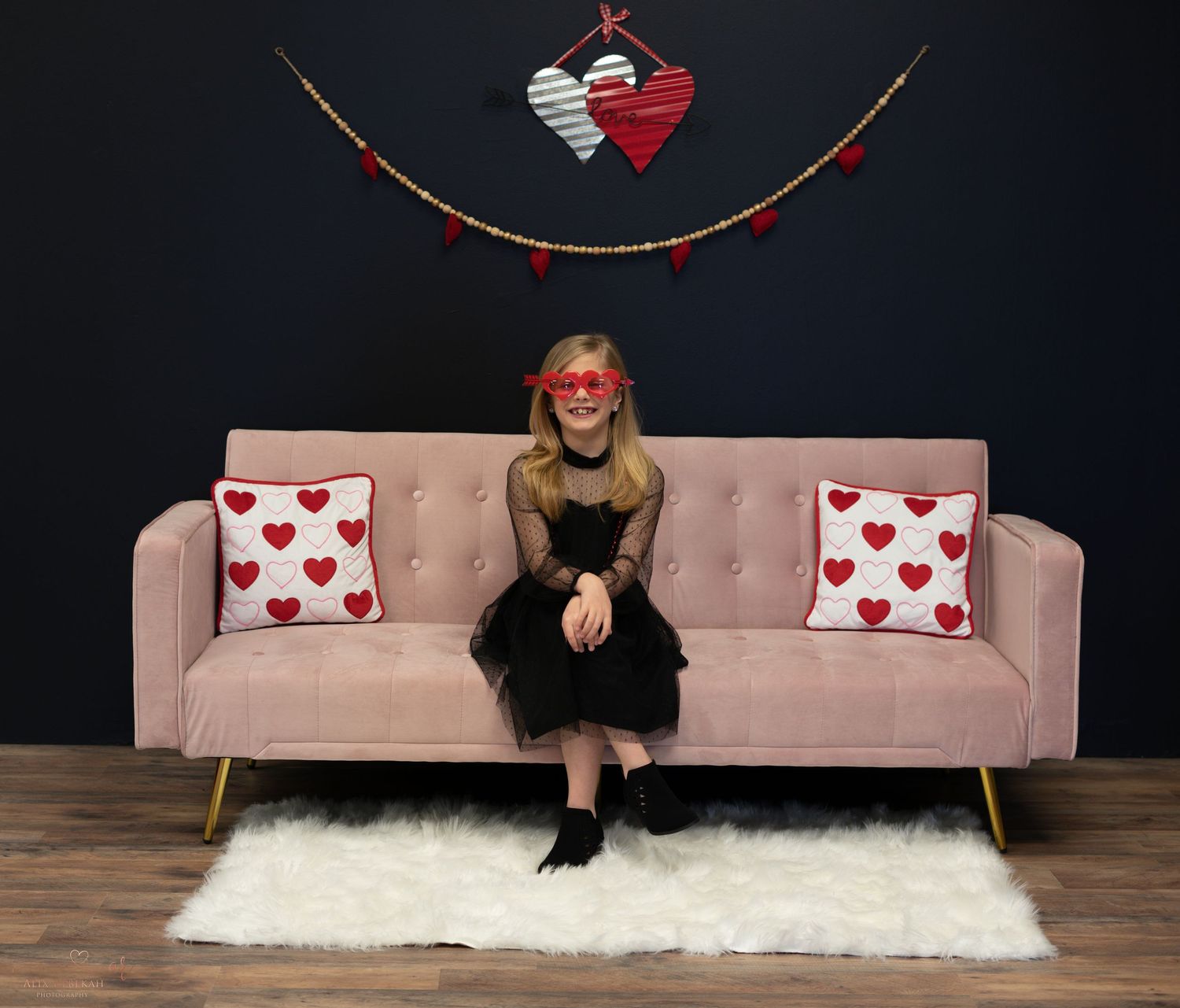 Pink velvet sofa with heart pillows and Valentine's Day decorations on dark backdrop.