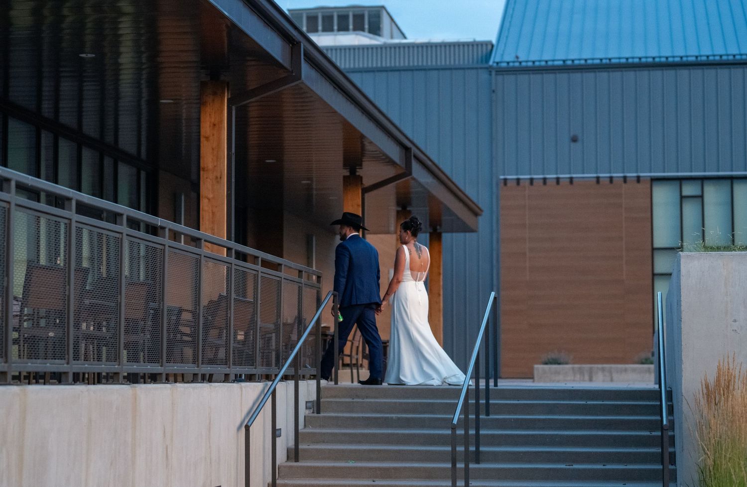 Bride and groom walking up outdoor stairs at modern building venue.