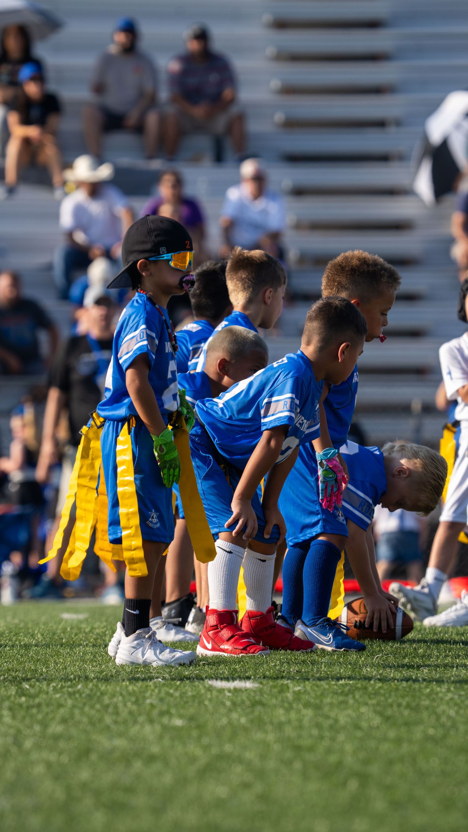 Soccer players in blue jerseys and yellow shorts sit on the sideline during a game.