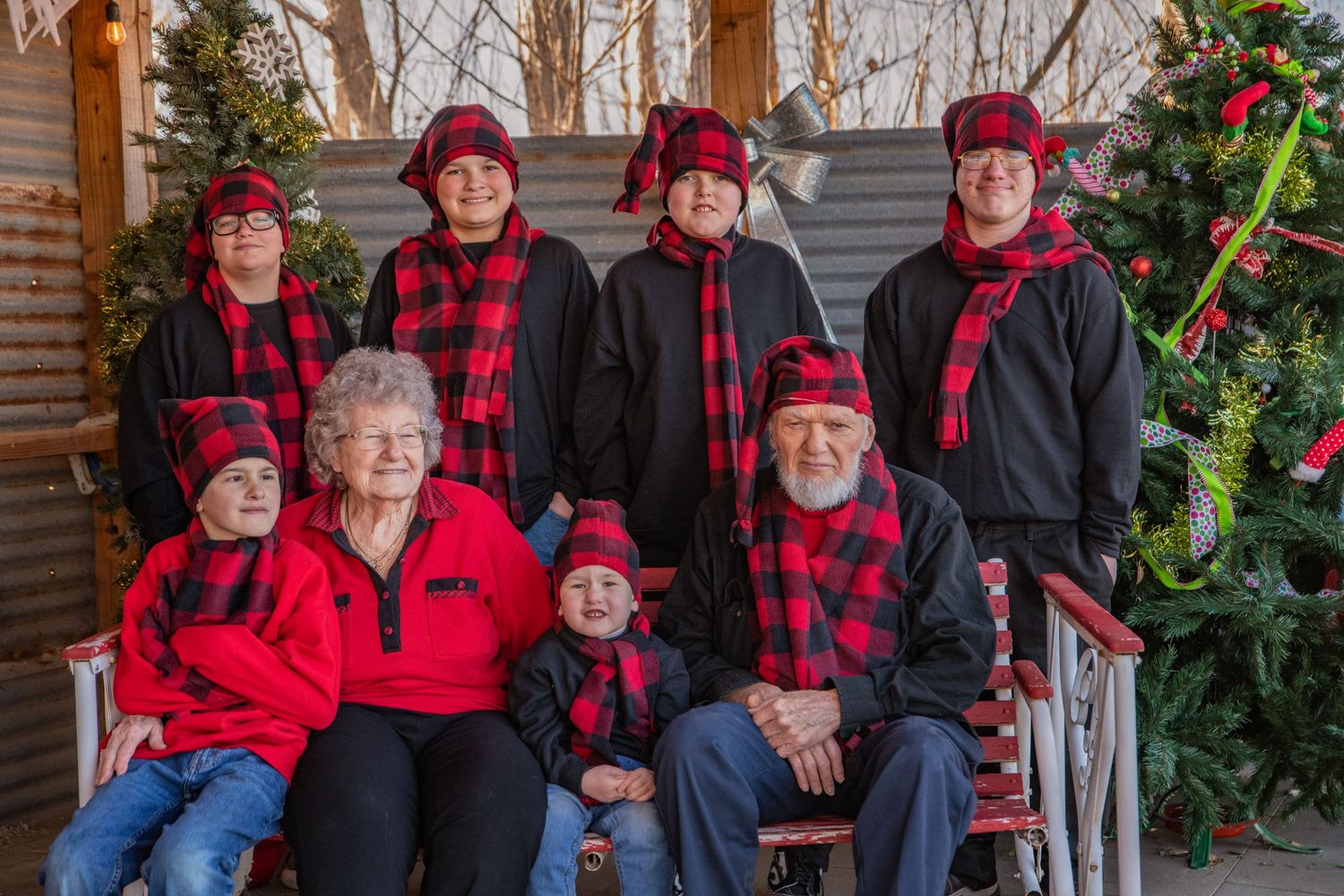 A group gathered in red and black buffalo plaid outfits poses by a decorated Christmas tree for a holiday portrait.