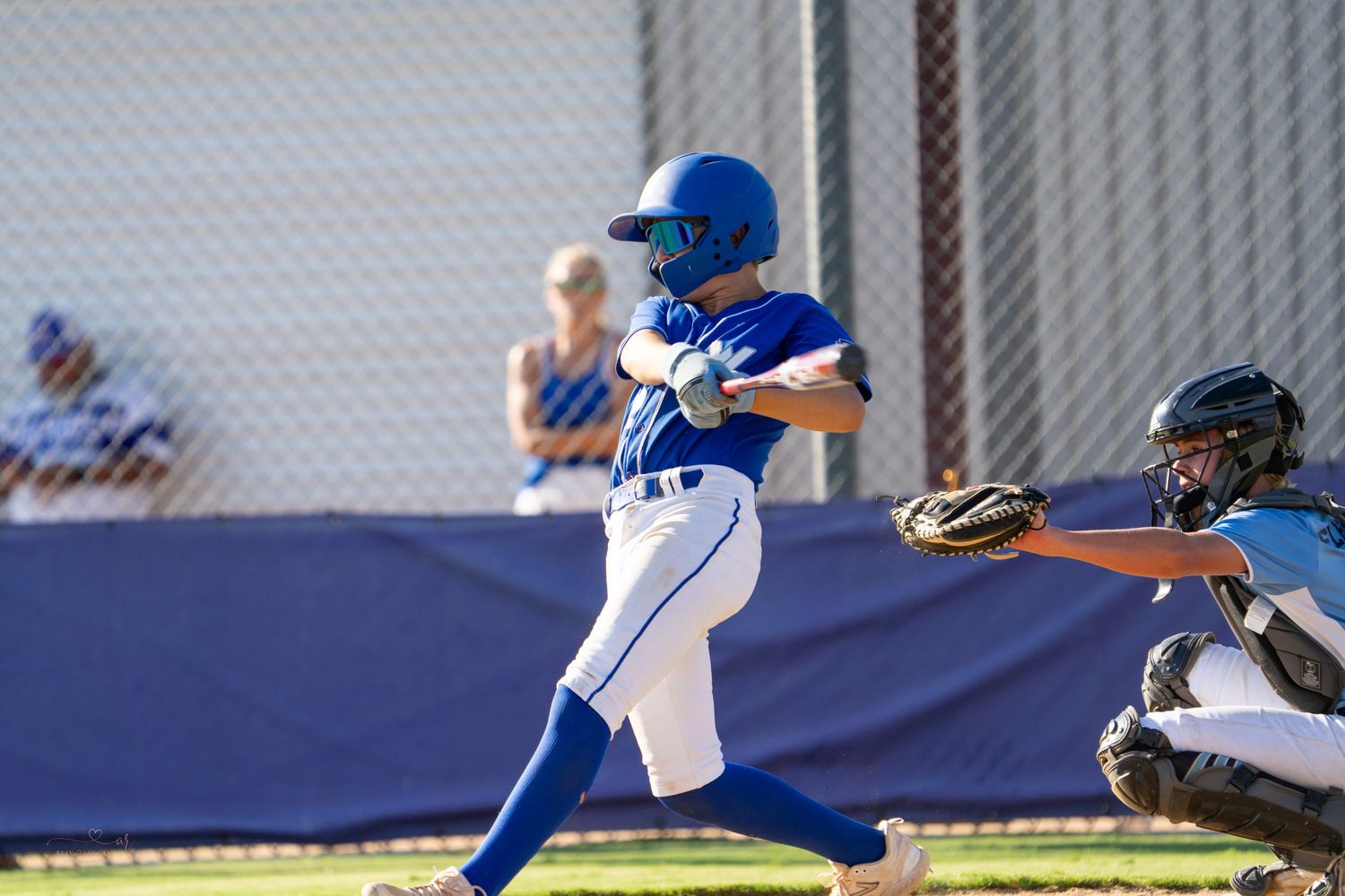 Baseball player in blue and white uniform swings bat during game while catcher prepares to catch behind home plate.