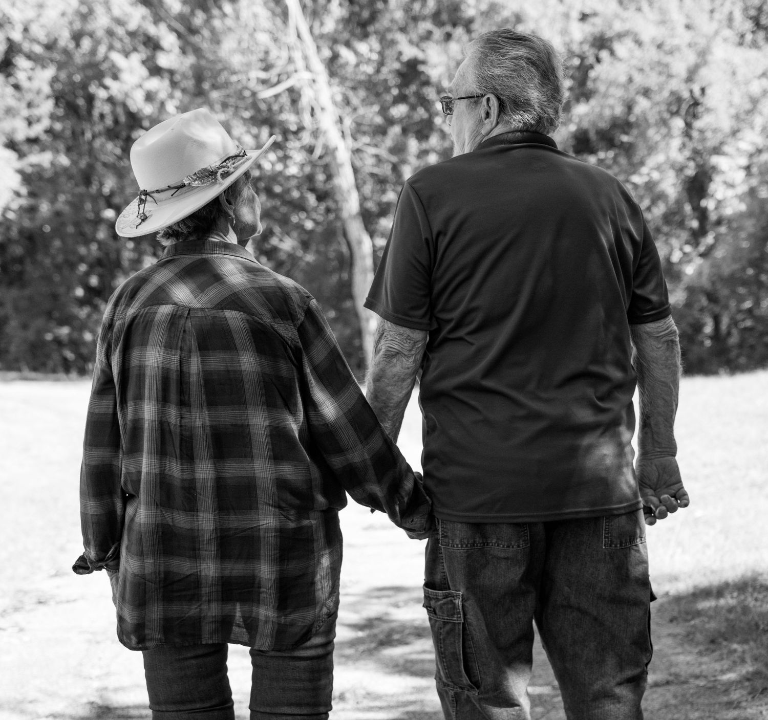 A black and white photo captures a couple walking hand in hand along a nature path.