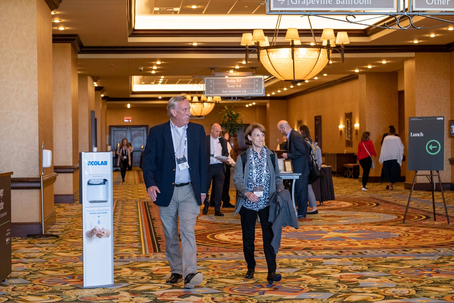 Attendees walking through a hotel conference center hallway with ornate lighting fixtures.