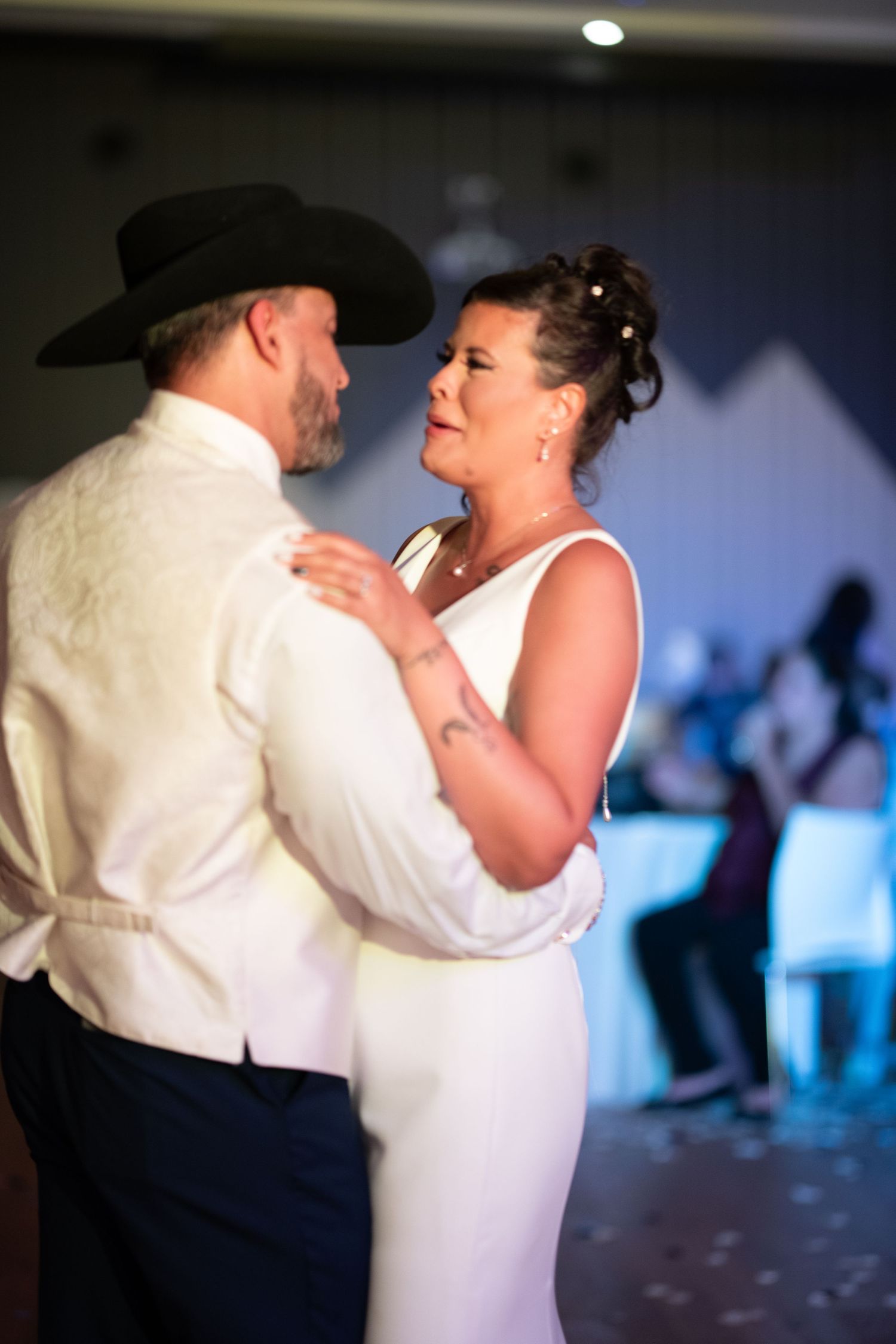 Romantic dance moment at wedding reception with soft lighting and couples dancing in background.