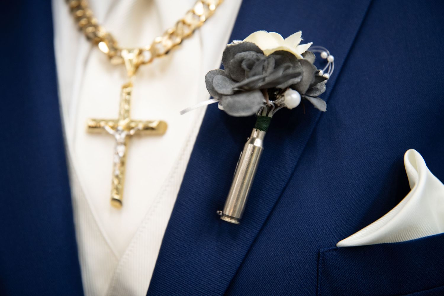 Gold cross necklace and dark floral boutonniere on navy blue suit jacket.