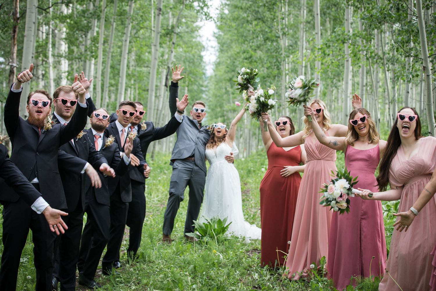 Wedding party poses playfully in an aspen grove with bridesmaids in pink dresses.