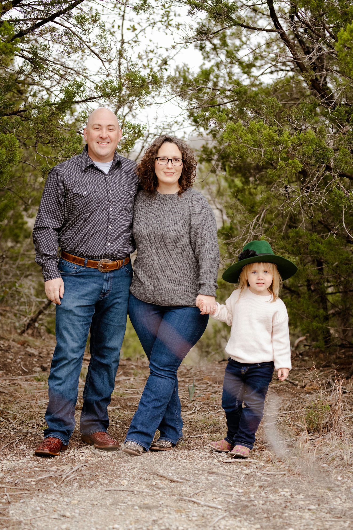 A family of three shown in a series of connected poses standing and crouching against a natural outdoor background.