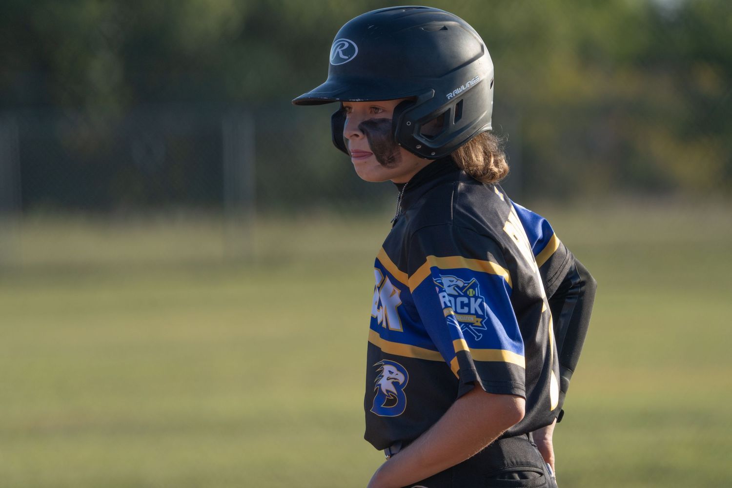 Softball player in blue and gold uniform with batting helmet stands ready during game.