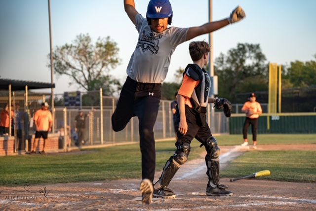 Baseball player makes dramatic leap while throwing the ball at sunset on baseball diamond.