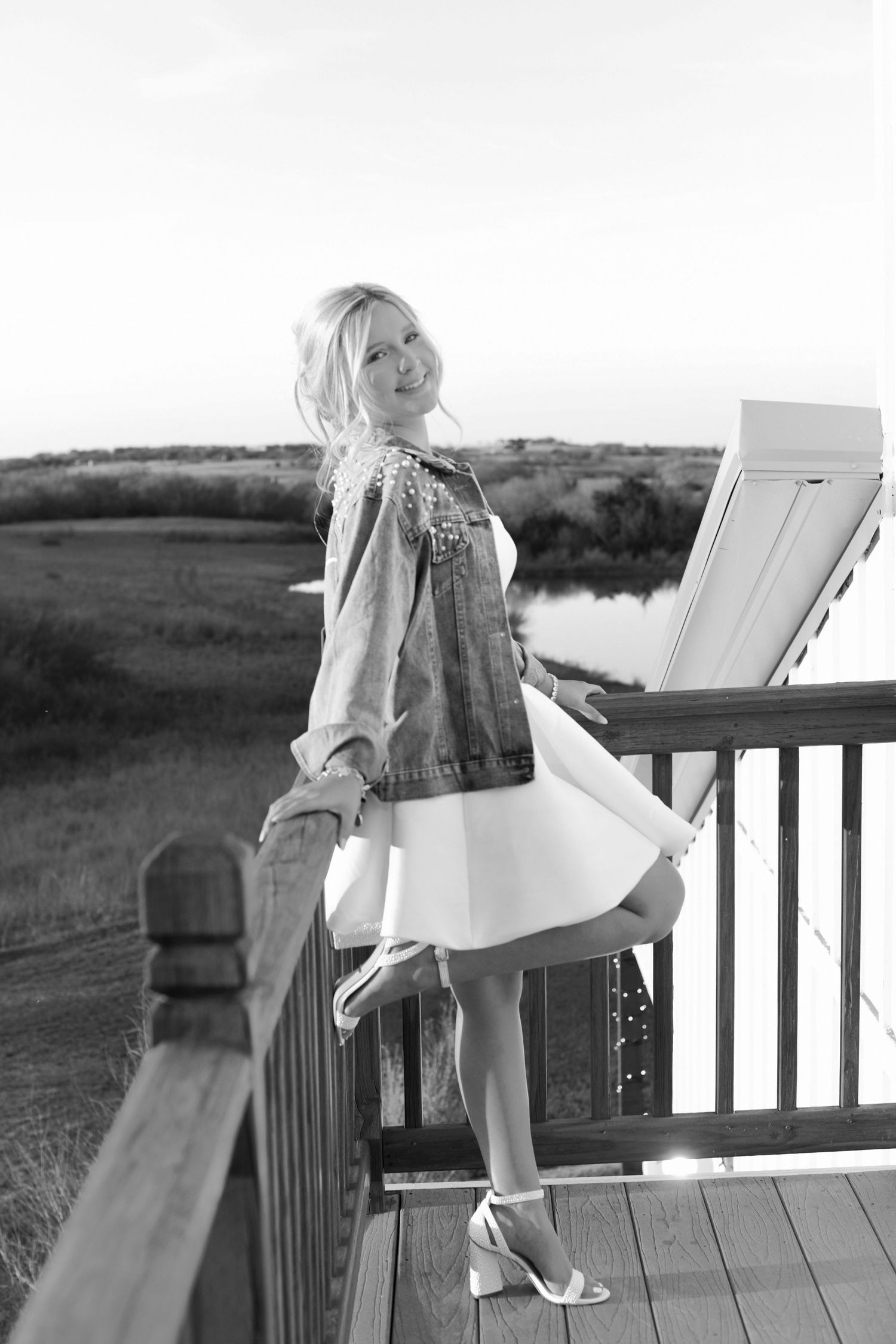 Black and white panoramic photo sequence of a person in a dress and heels posing on a deck railing at sunset.