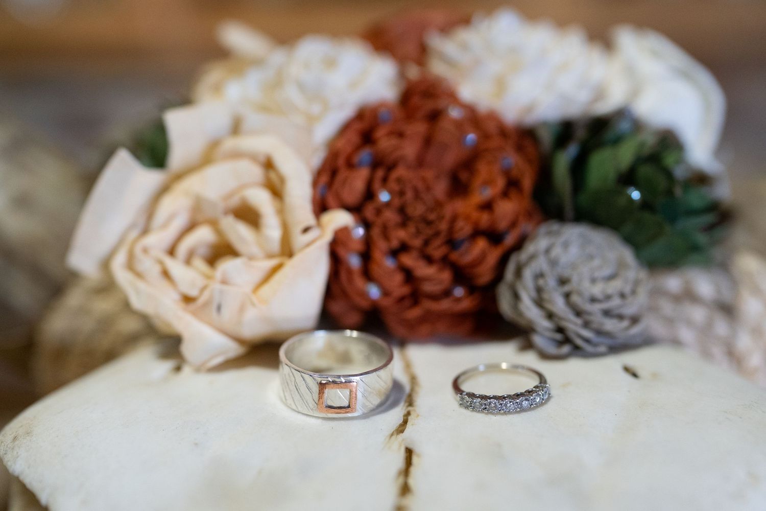 Two wedding rings displayed with vintage-styled fabric flowers in muted tones.
