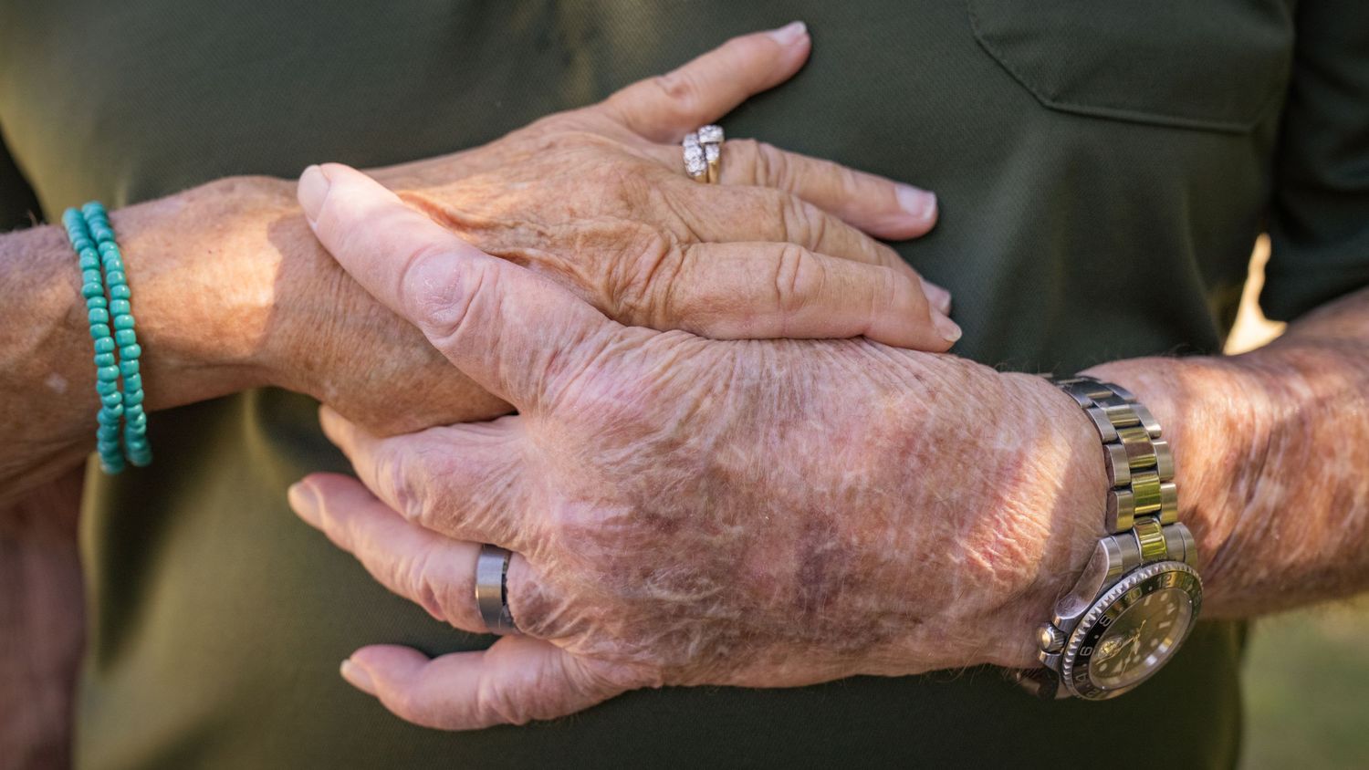 Close-up of weathered hands with jewelry tenderly clasped together.