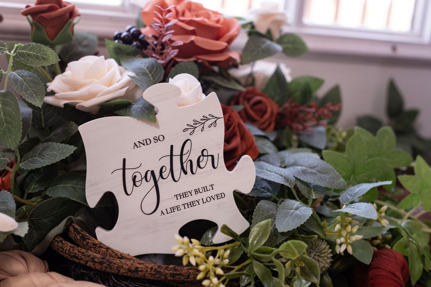 A romantic 'together' sign nestled among pink and burgundy roses with green foliage in a rustic setting by a window.