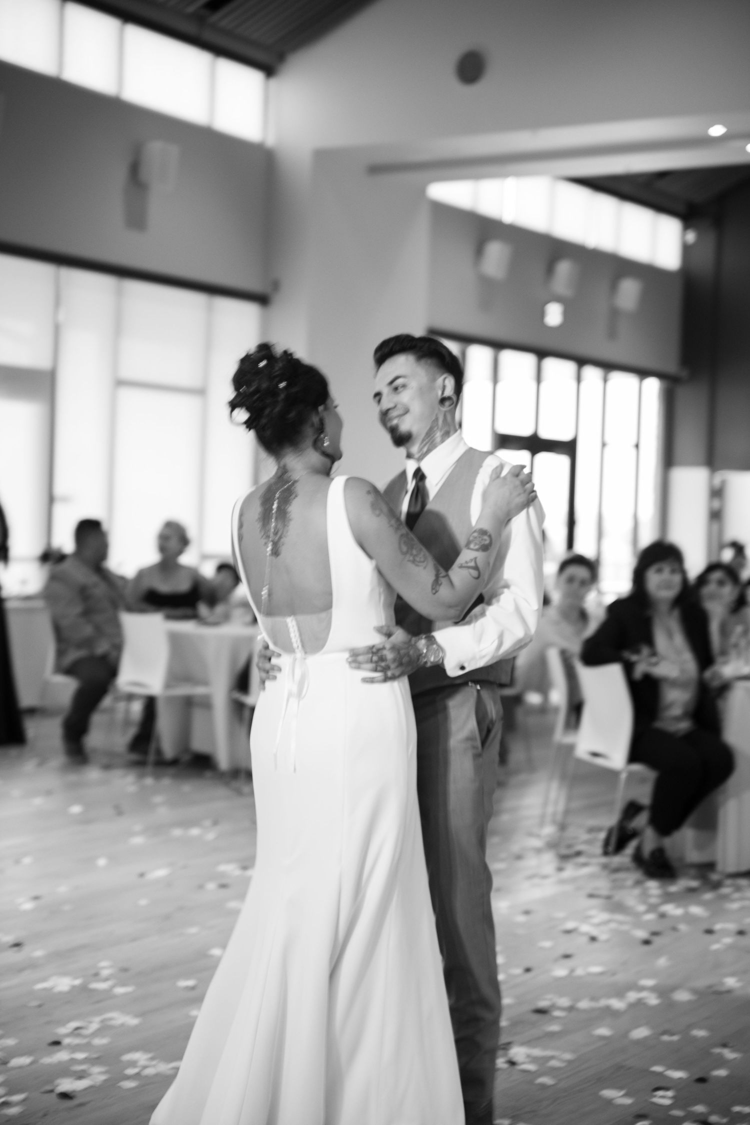 Couple shares their first dance in an elegant reception hall with scattered petals on the floor.