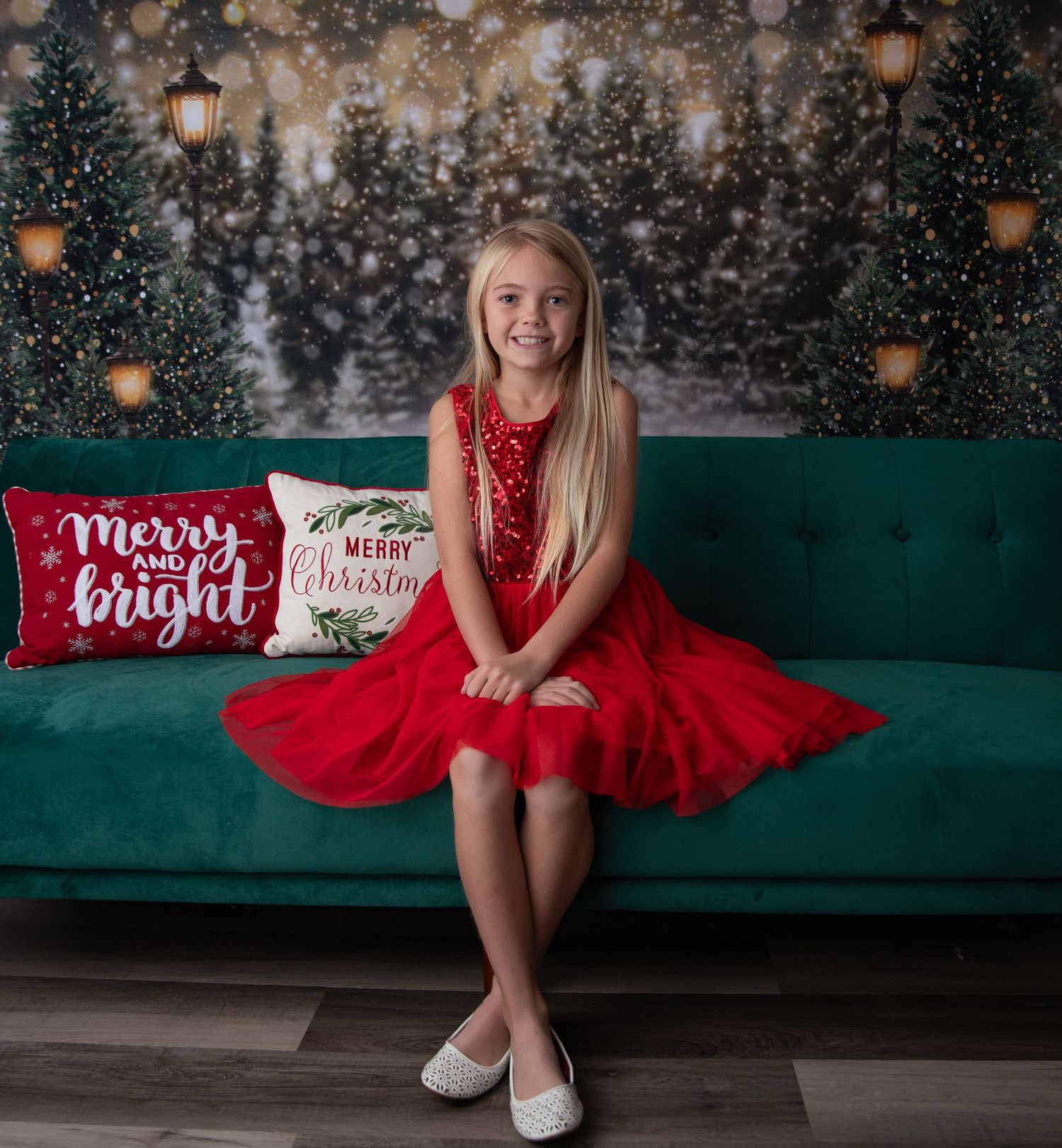 A child in a red holiday dress poses on a green couch with festive pillows.