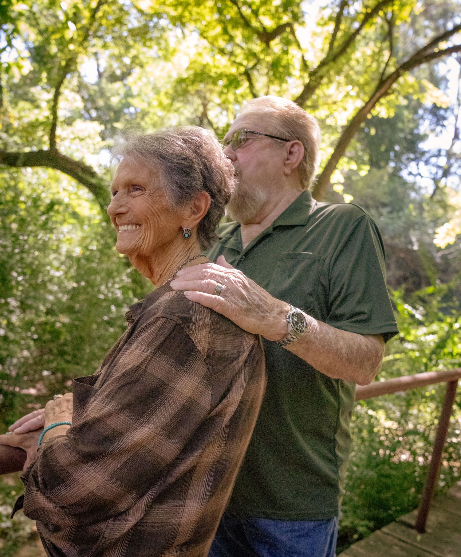 A loving moment shared between two people on a wooden walkway in dappled sunlight.
