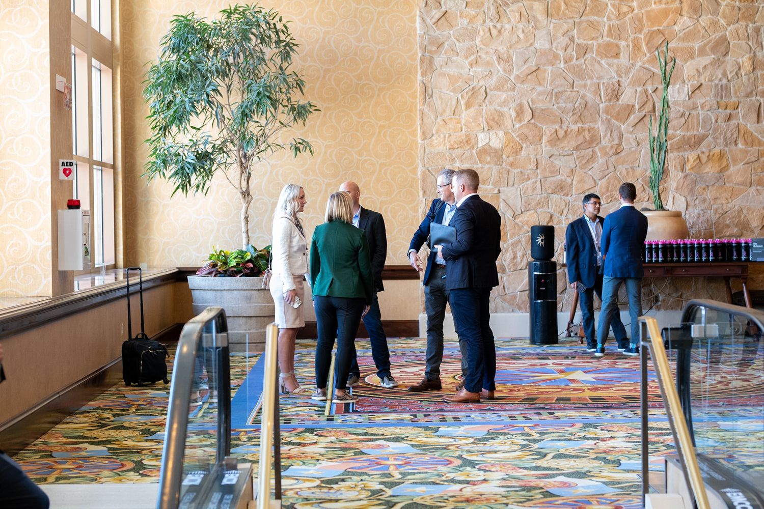 Conference attendees gathering in a hotel lobby area with stone walls and decorative carpeting.