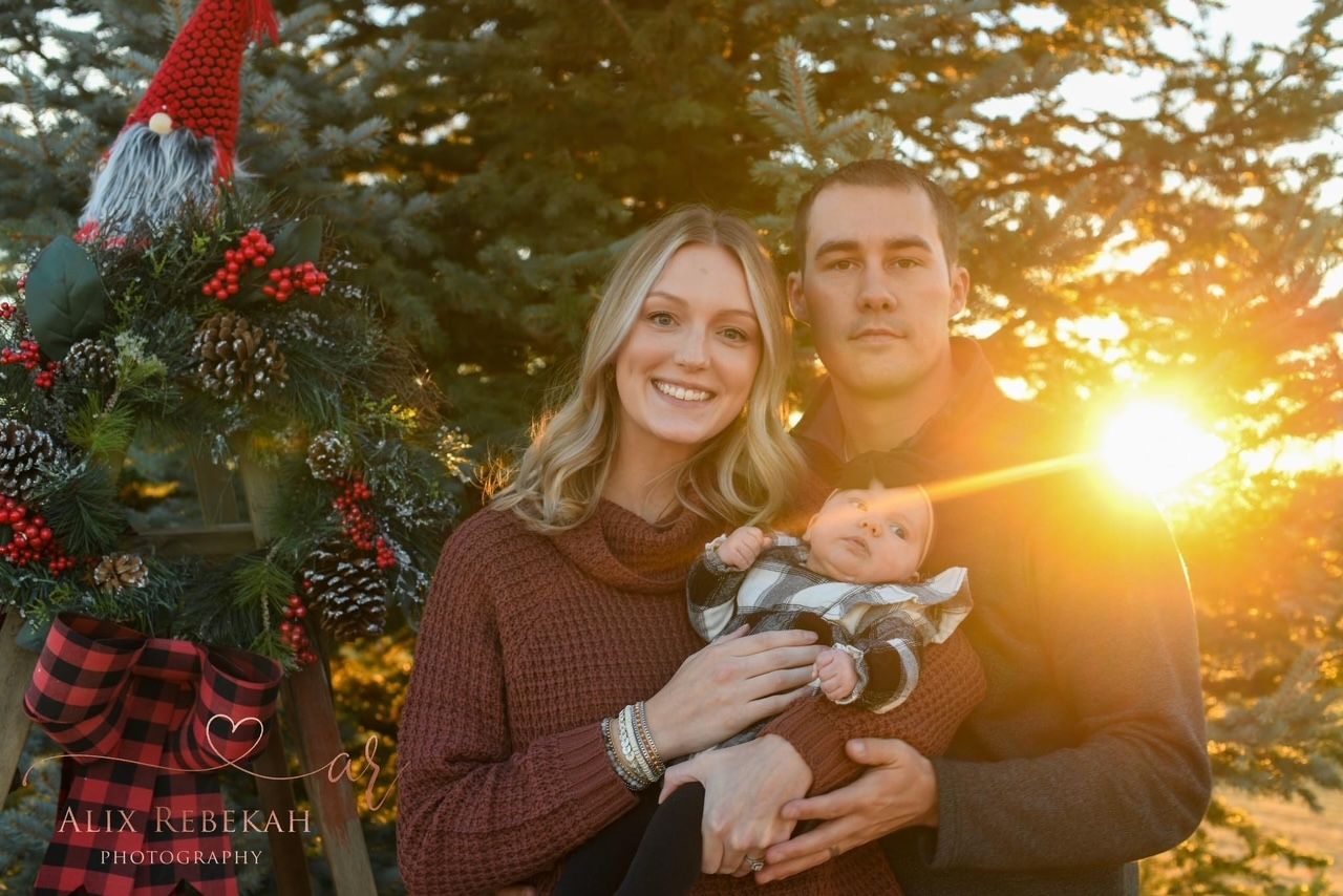 Family portrait at sunset in front of Christmas tree outdoors.