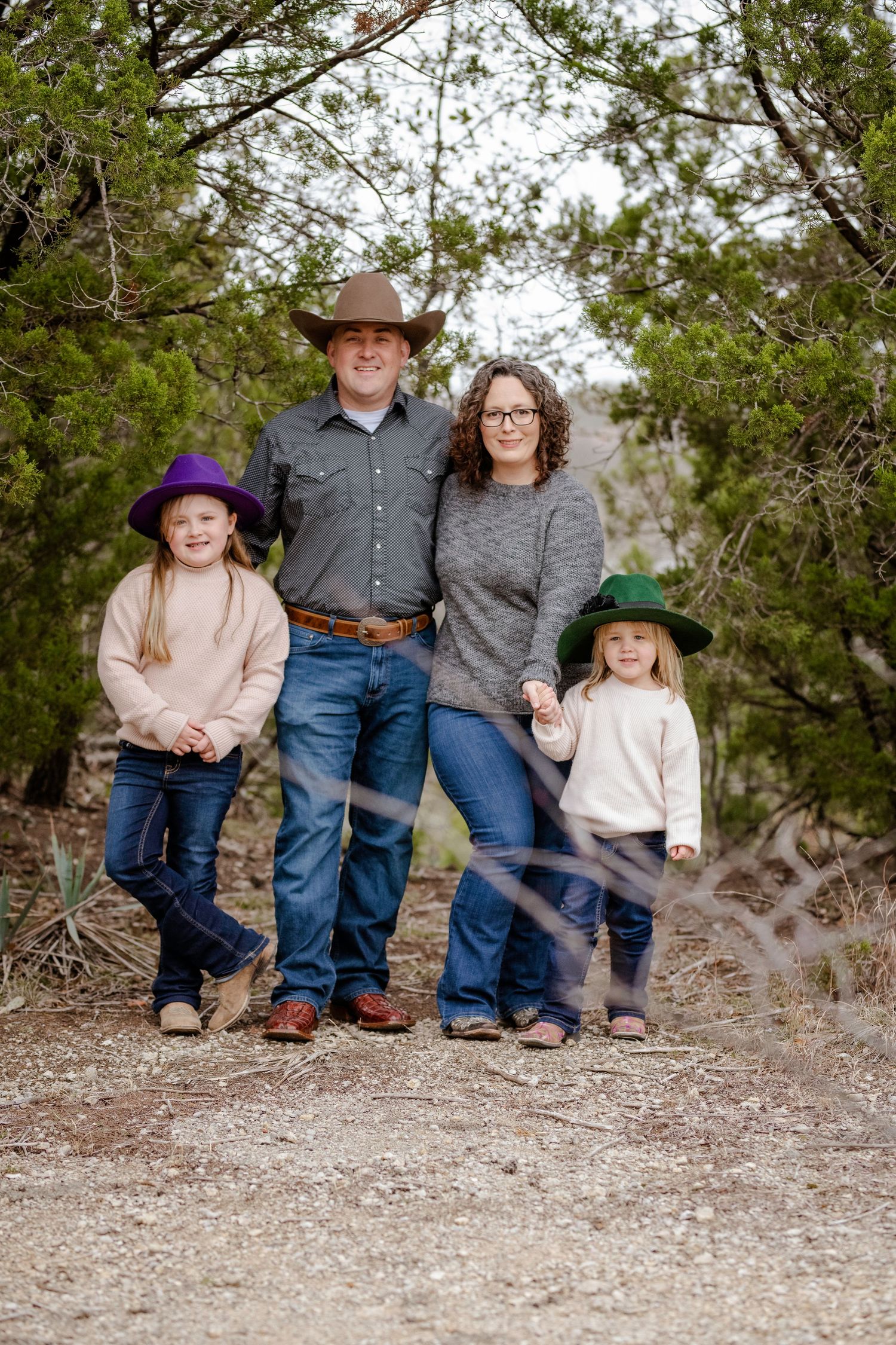 Family in casual western wear sitting together on a rocky ground in a natural outdoor setting.