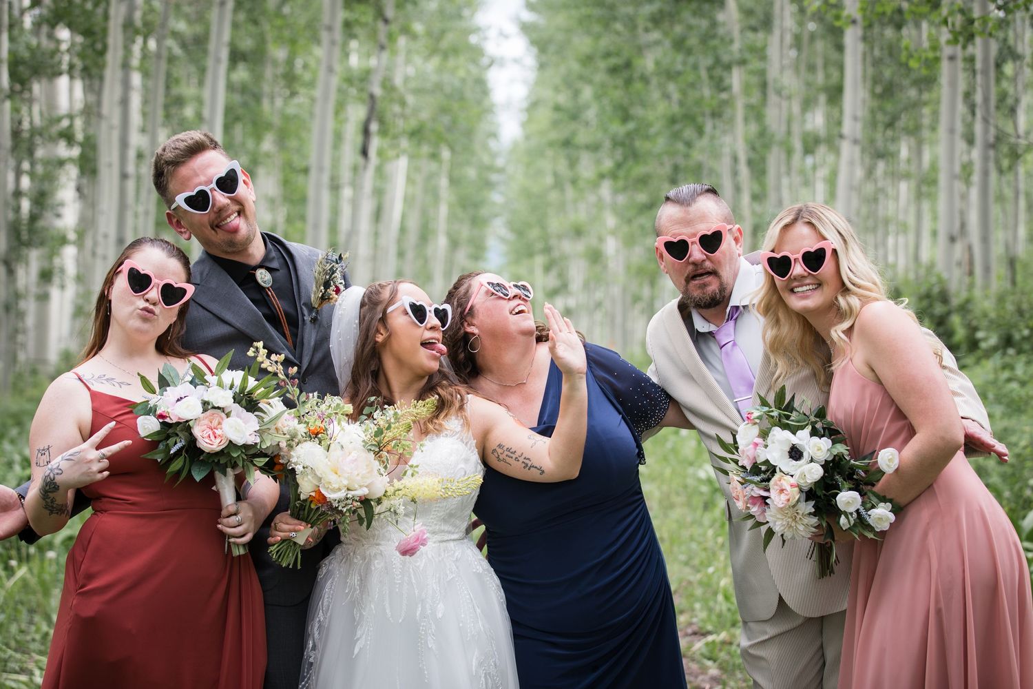 Wedding group wearing sunglasses poses joyfully among aspen trees.