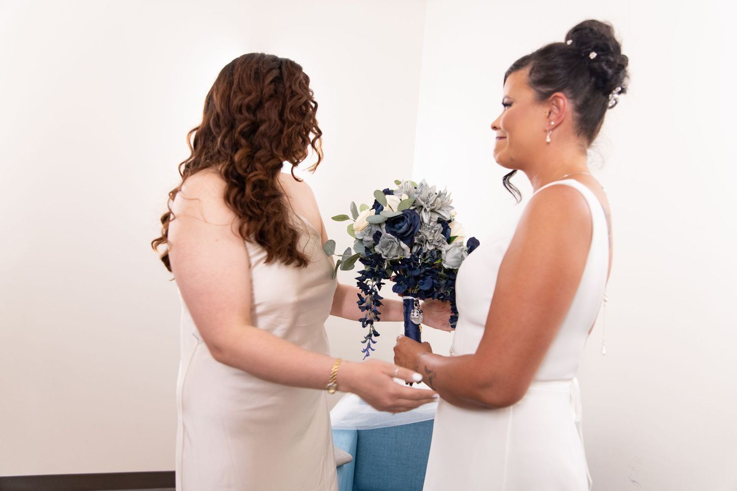 Two people in white dresses holding a blue and white floral bouquet.