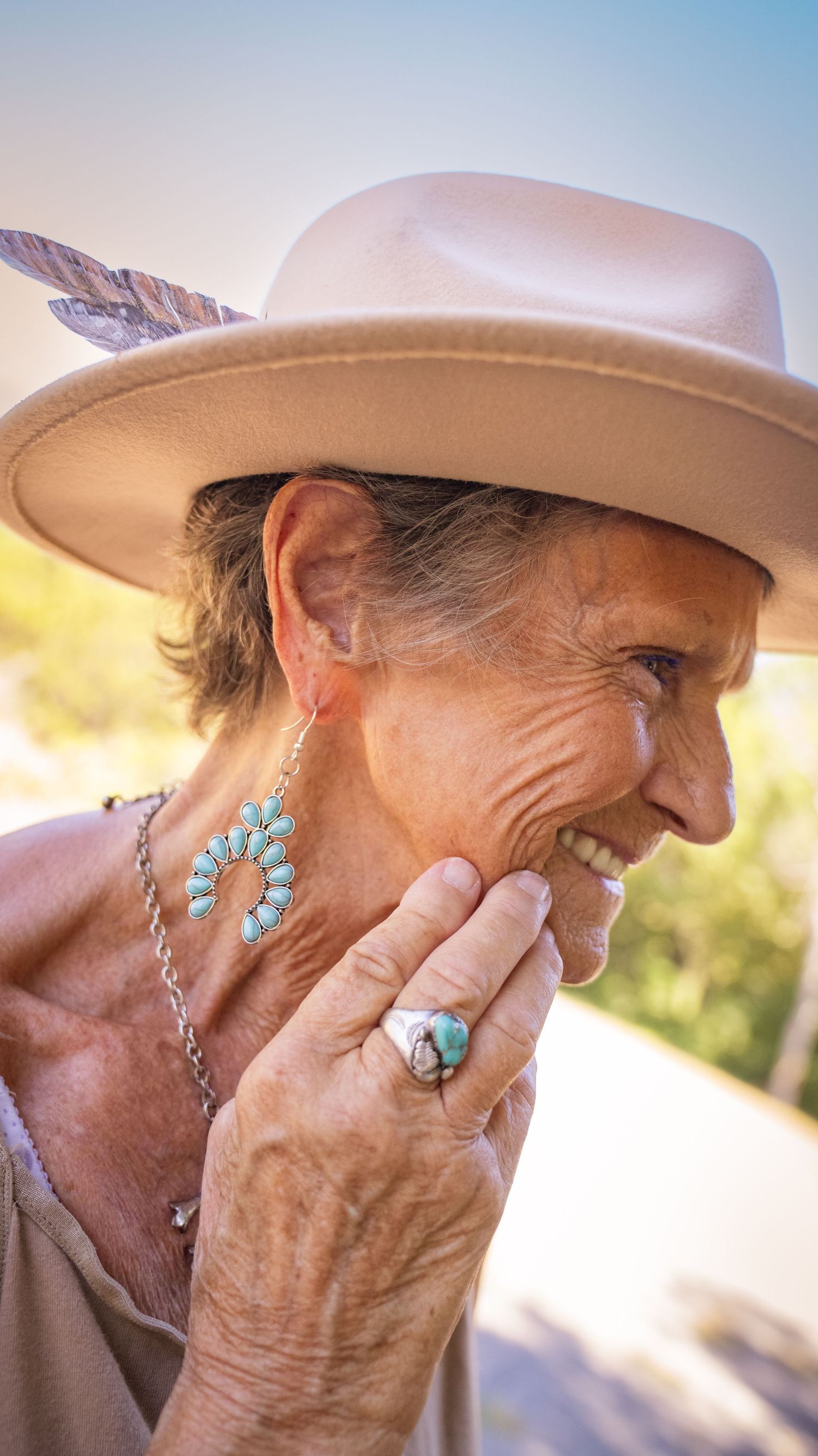 Person wearing turquoise jewelry and tan hat laughs joyfully in warm sunlight.