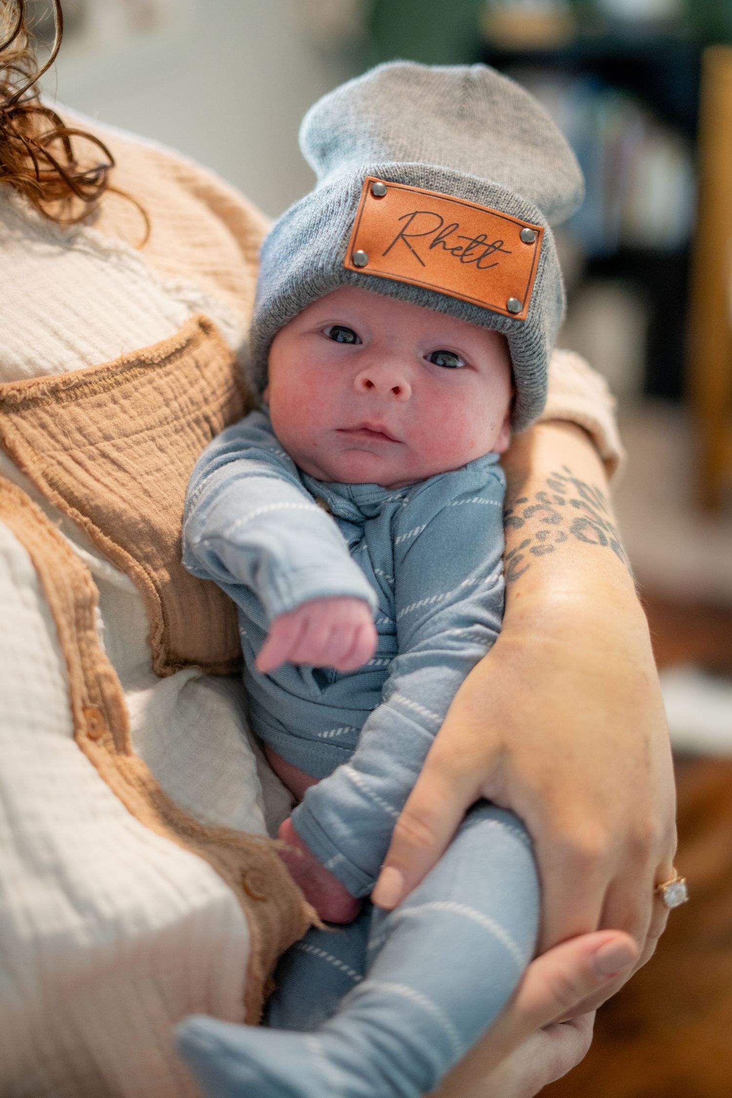 A tiny baby wearing a gray beanie and onesie is cradled in gentle arms.