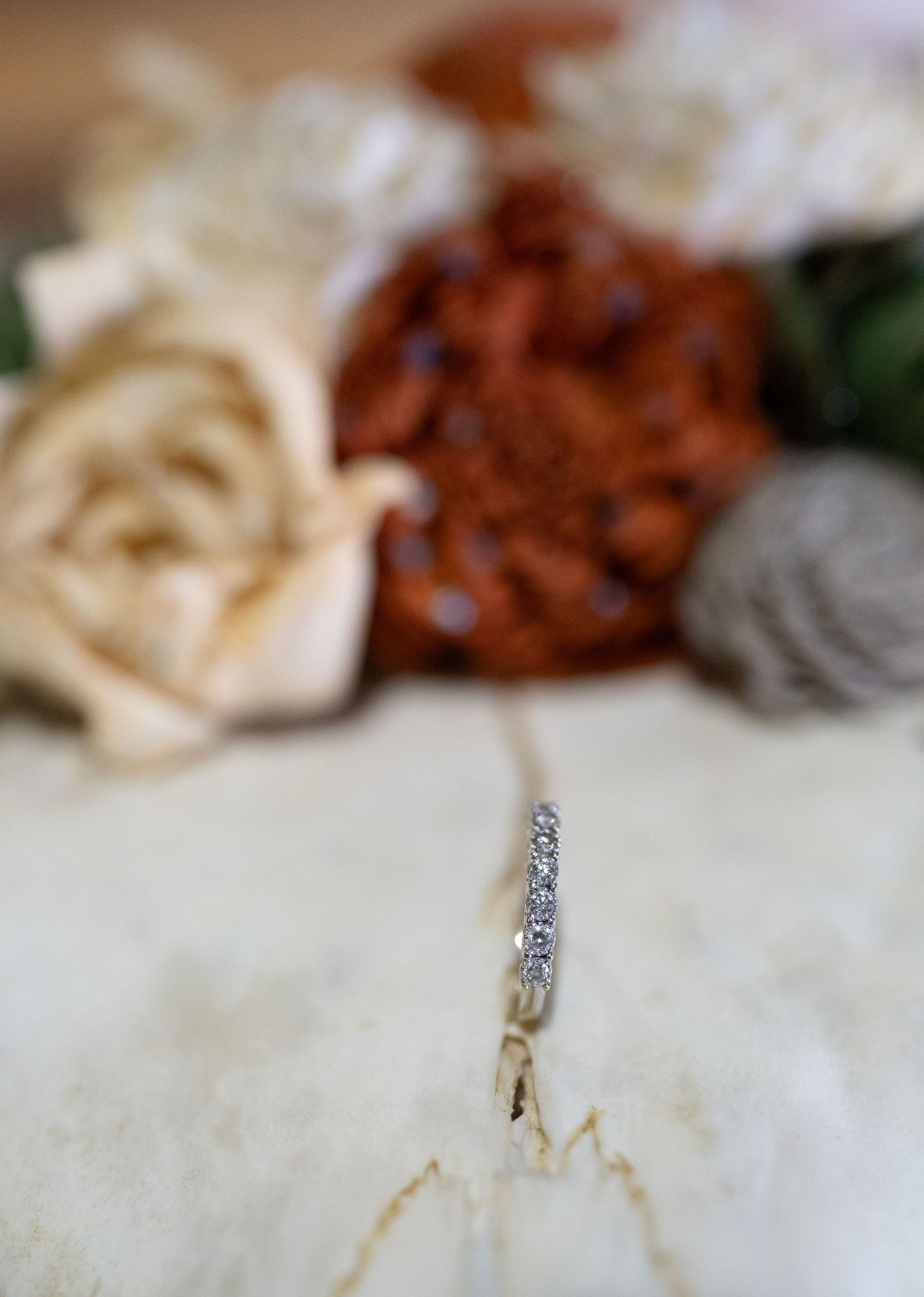 A diamond wedding ring photographed with soft floral decorations in the background.