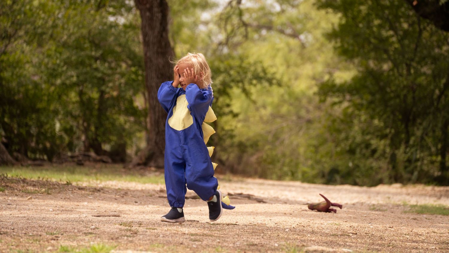 A small child in blue overalls running on a dirt path through nature.