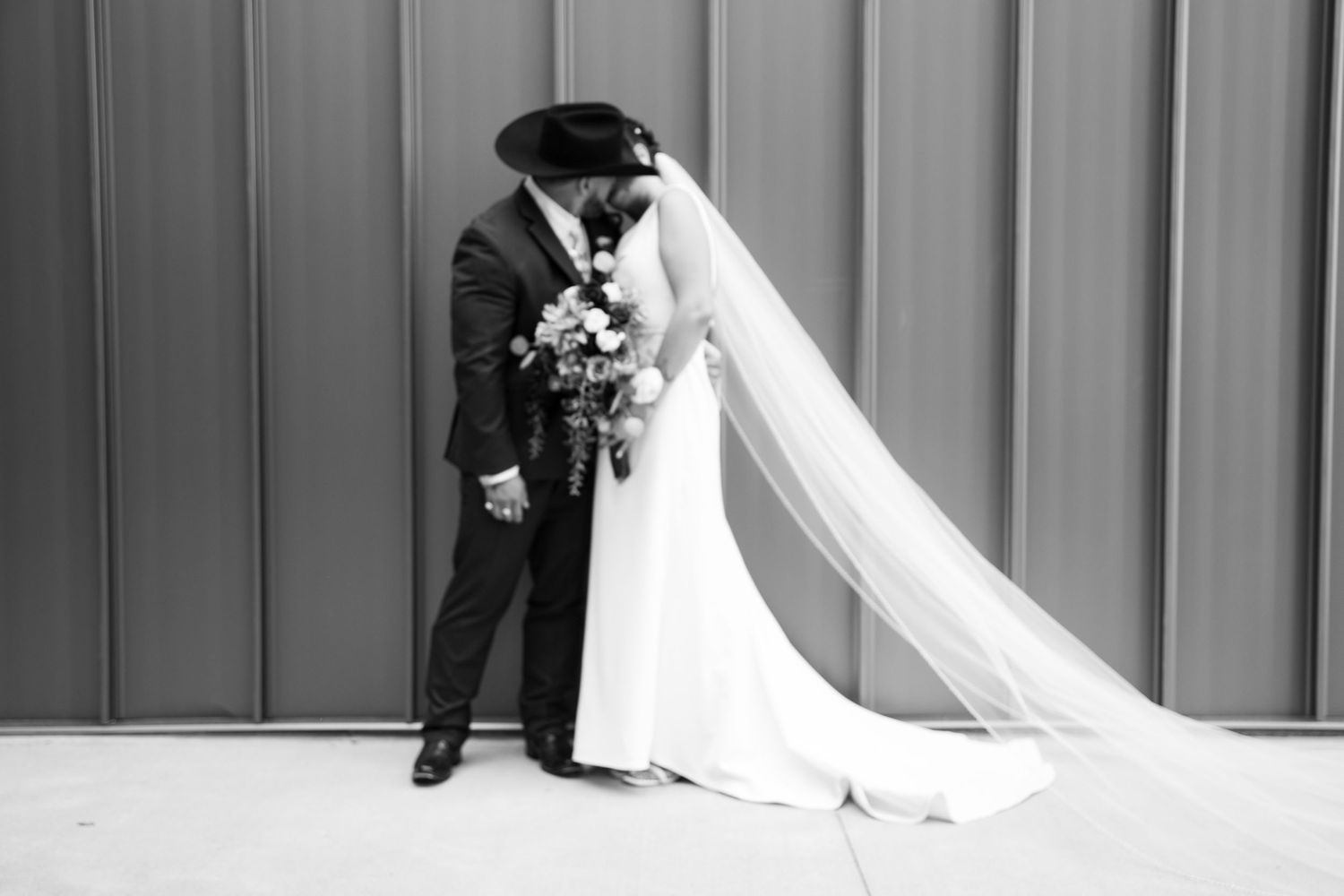 A black and white wedding portrait showing a romantic moment against a modern wall backdrop.