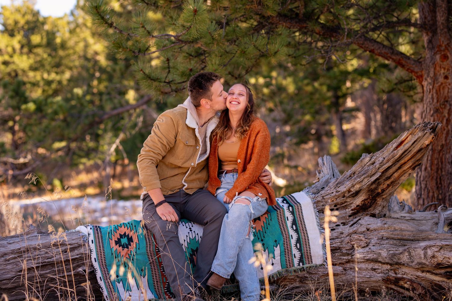 Couple sitting together among large fallen trees in a scenic mountain forest setting during golden hour.