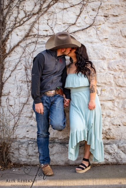 Romantic couple in western wear embracing against white stone wall.