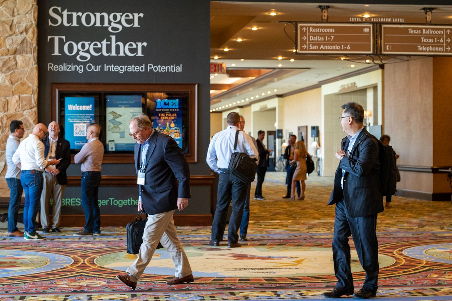 Conference attendees networking in a hotel hallway with a 'Stronger Together' banner displayed.
