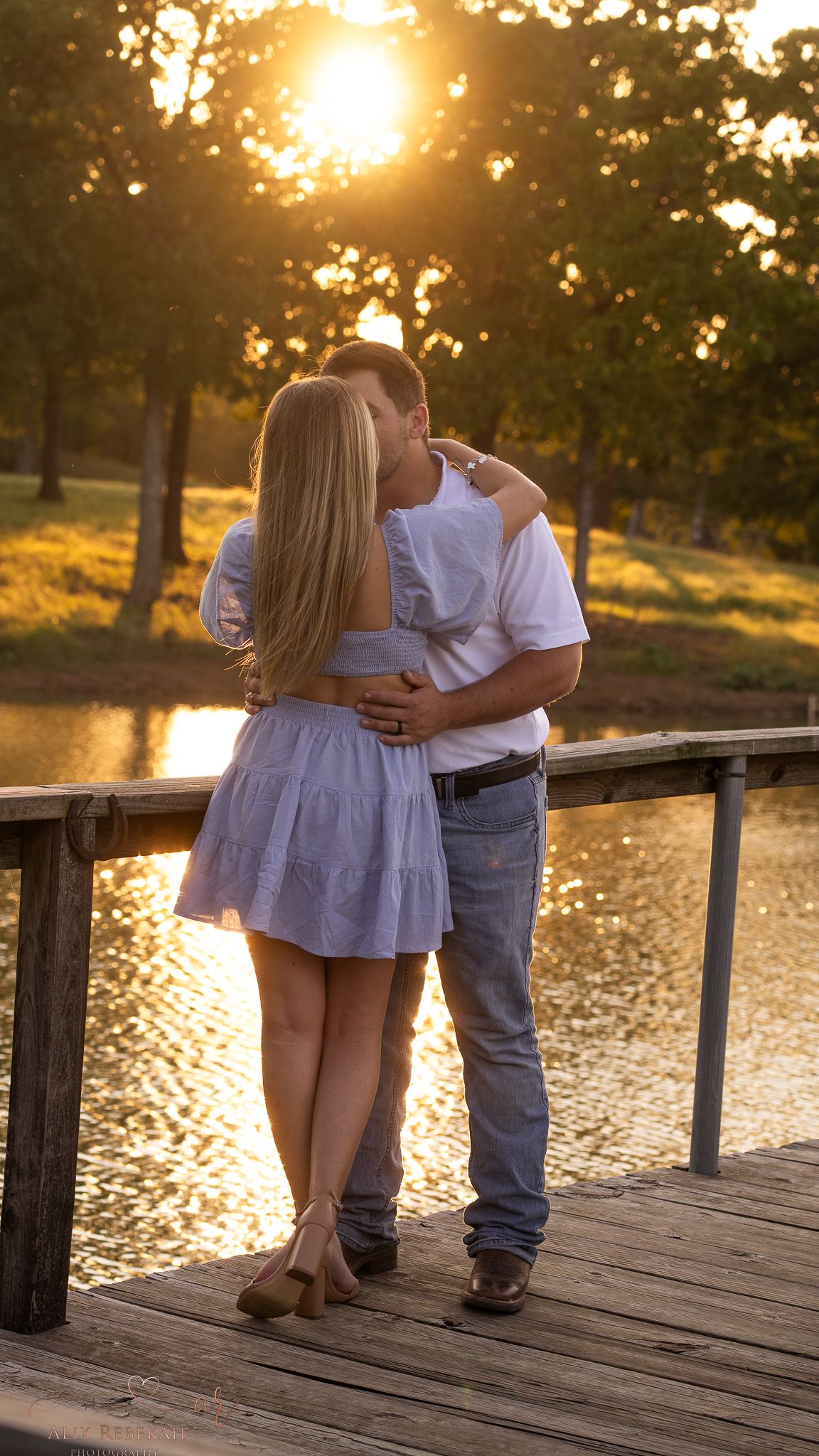 A romantic sunset moment shared on a wooden dock overlooking reflective water.