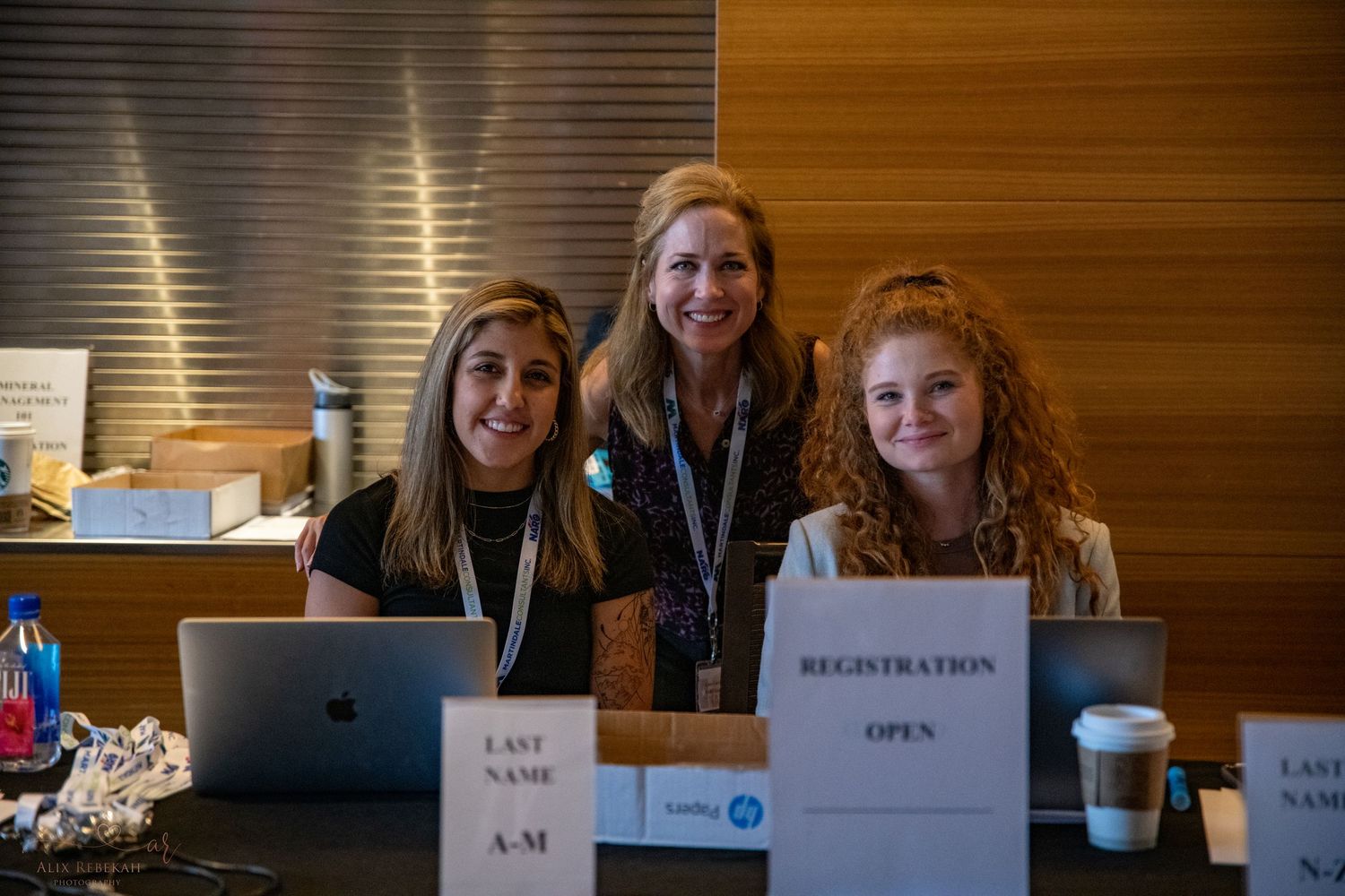 Three staff members sit at a registration table with laptops during an event.