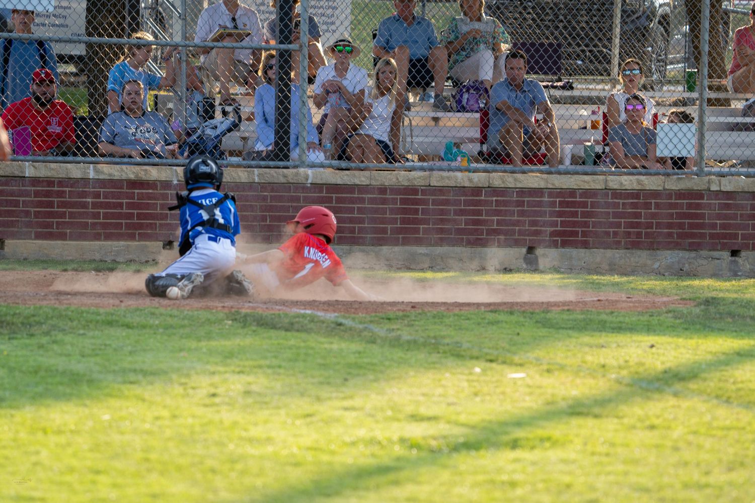A baseball player in uniform slides into home base during an intense game at a local baseball field.