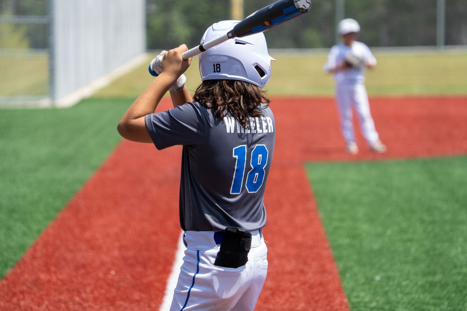 Baseball player in light blue jersey number 18 stands at bat on red turf field during game.