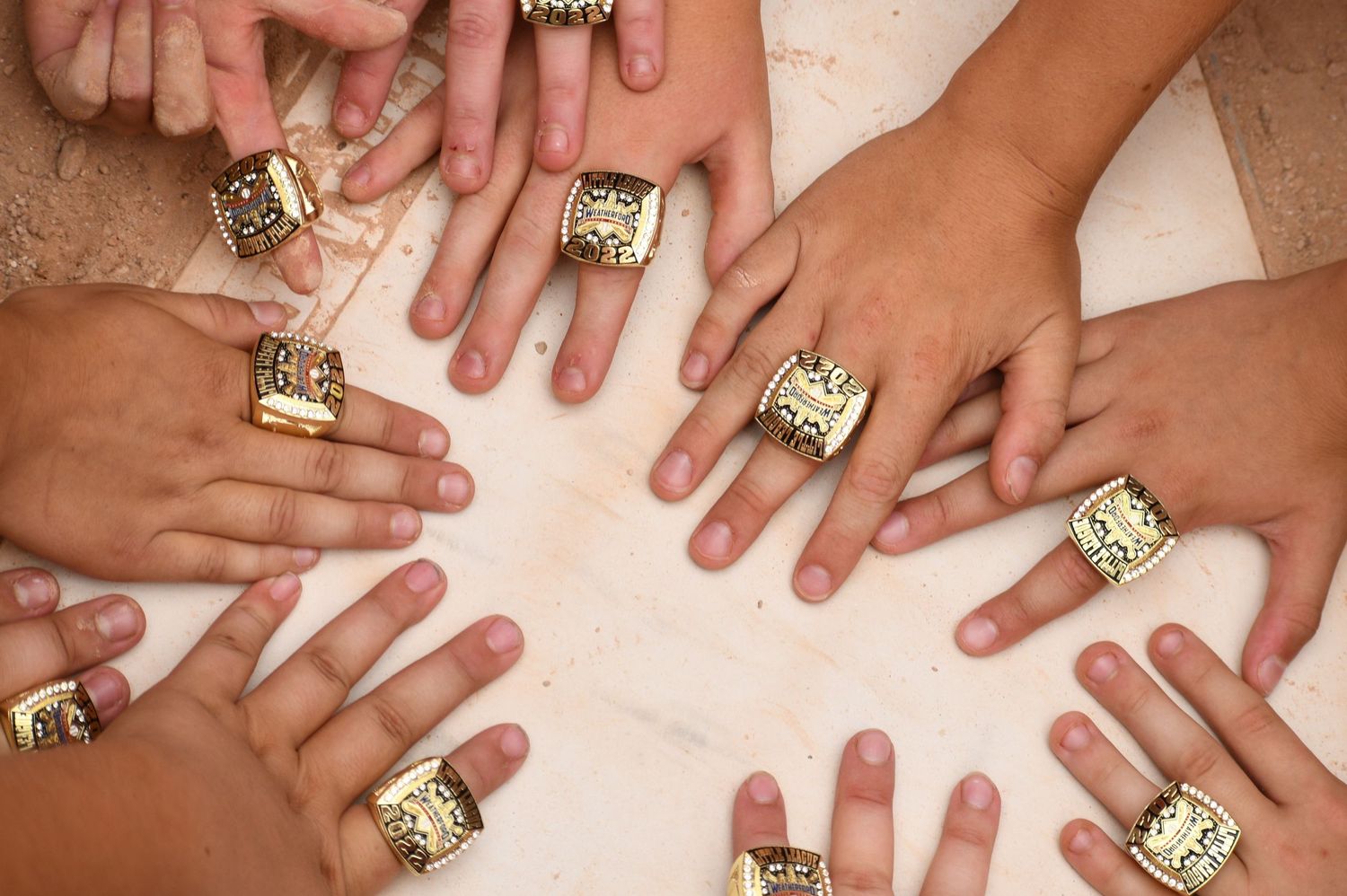 Hands in a circle showing off matching gold championship rings against a soft neutral background.