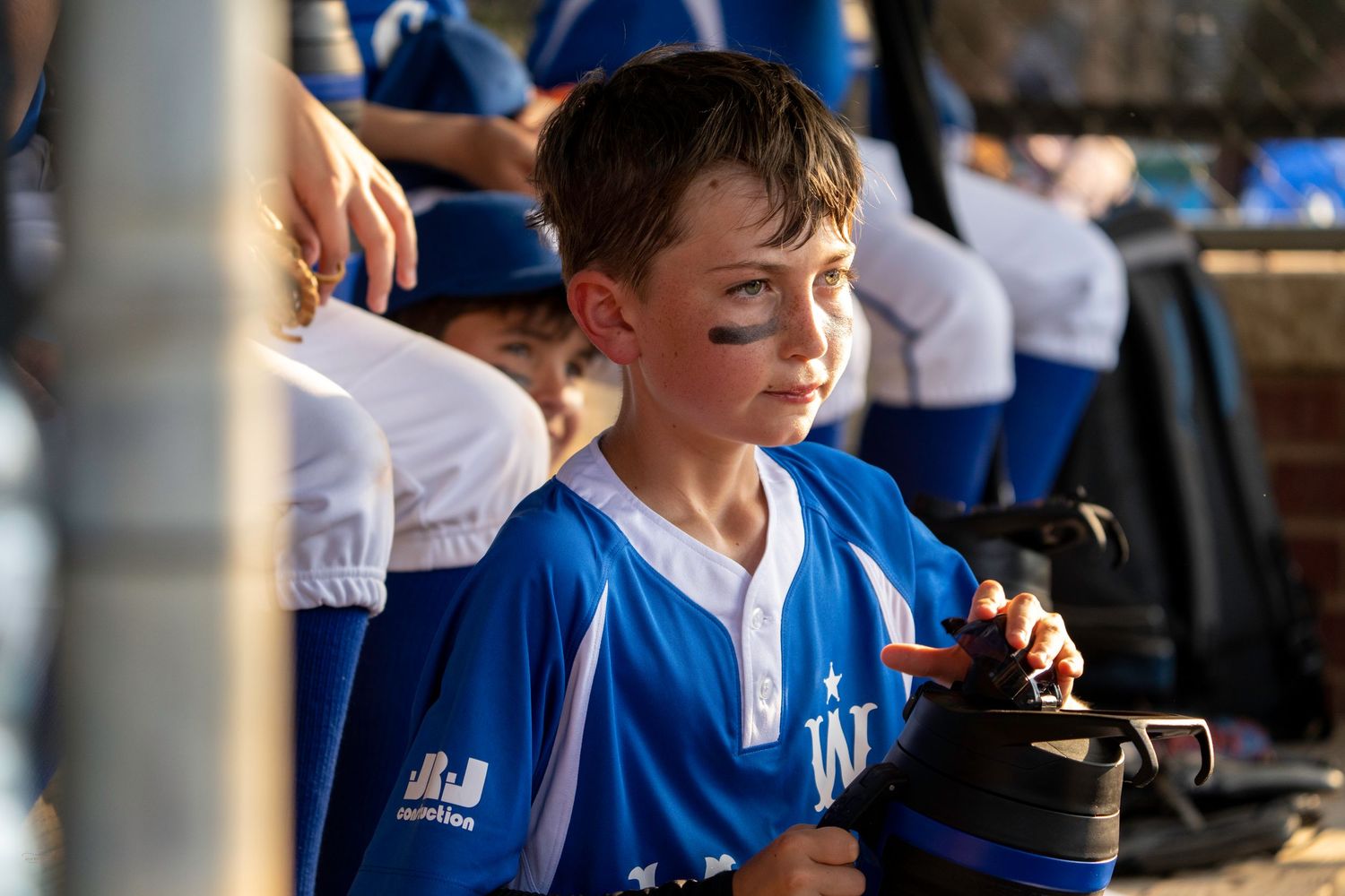 Boy in blue jersey at sporting event smiling and laughing with friends in the crowd.