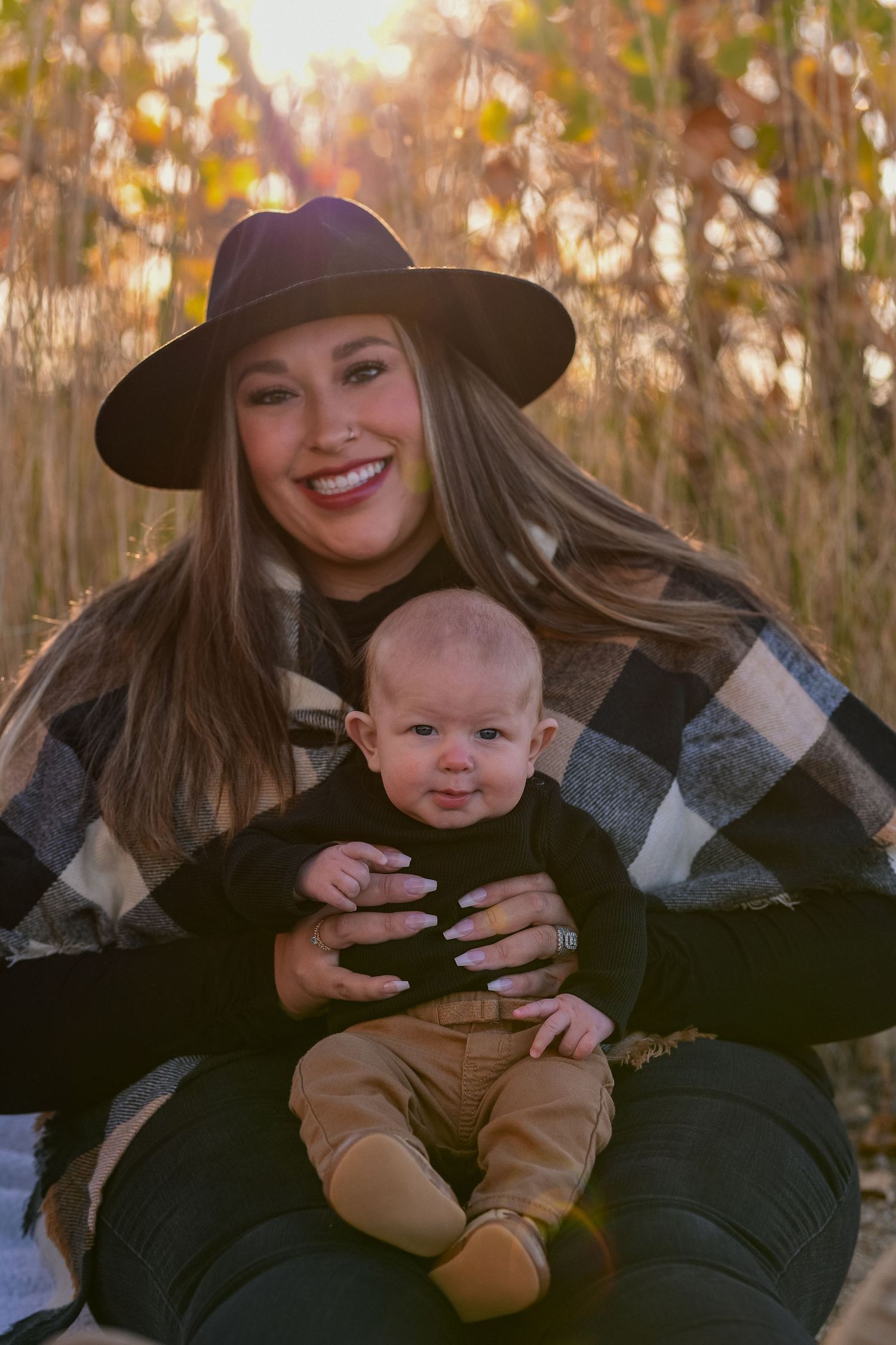 Fall outdoor portrait with woman in hat and plaid poncho holding baby in casual wear.