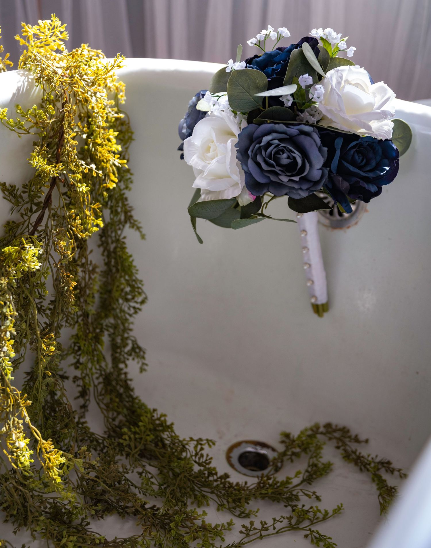 Wedding bouquet with navy blue and white roses next to yellow flowers in a white bathtub.
