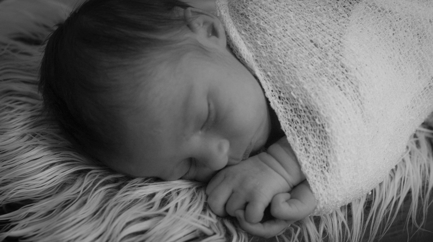 Close up of sleeping baby wrapped in soft white blanket.