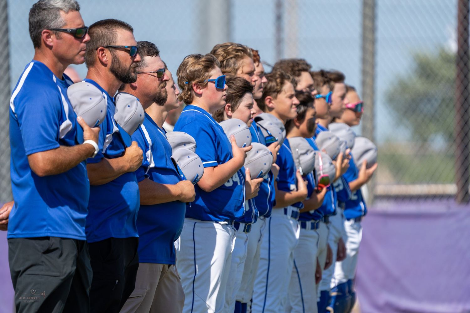 Baseball team lined up on field wearing blue uniforms during national anthem.