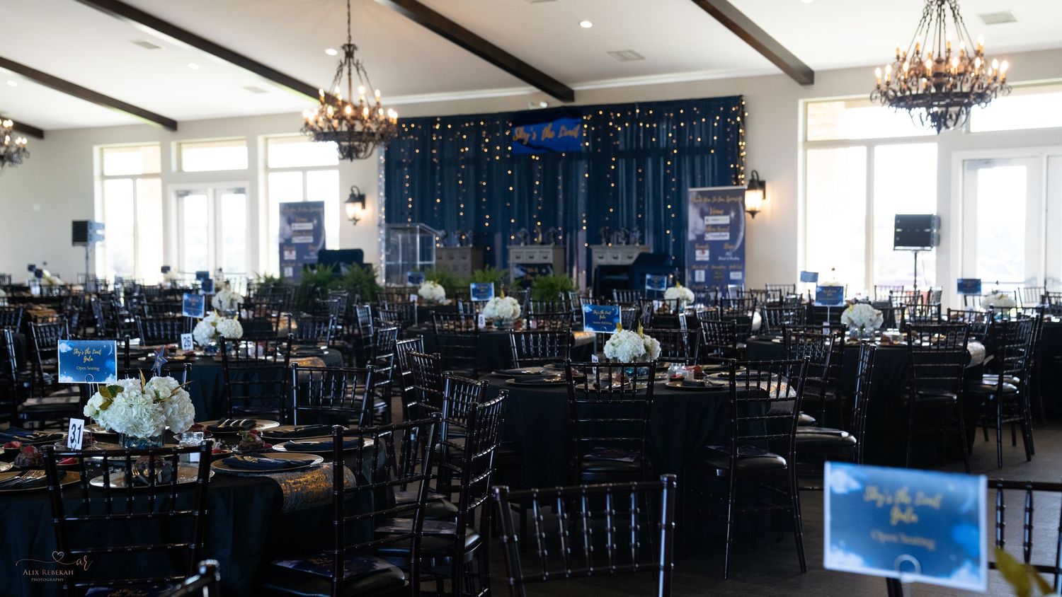 Large ballroom set up with black chairs and tables for formal evening celebration.