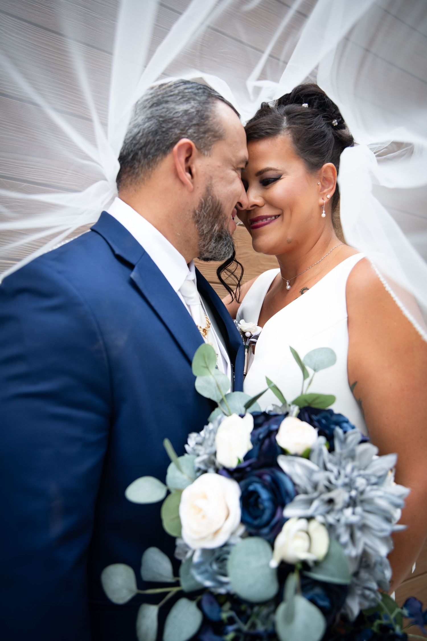Intimate wedding portrait with navy and white floral bouquet under flowing veil.
