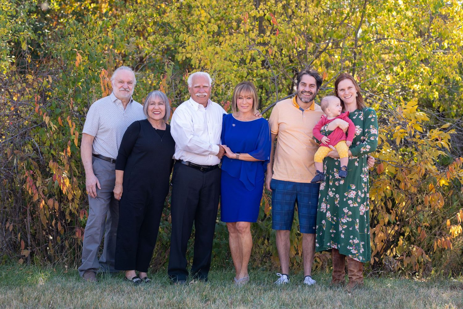 Group poses together in front of vibrant yellow autumn foliage during outdoor photo session.